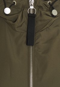 Oliwkowa kurtka z zamkiem błyskawicznym z przodu, z metalowymi akcentami w kolorze srebrnym, elastycznym kapturem na sznurku oraz gładką, błyszczącą fakturą.