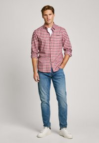 Red and white checkered long-sleeve shirt, blue jeans, and white sneakers. The shirt has a button placket and buttoned cuffs.