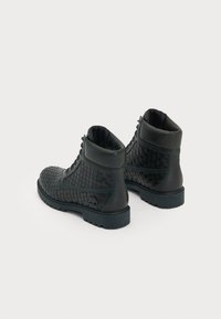 Black leather boots feature a woven design, rounded toe, ankle height, and textured rubber sole with visible grip.