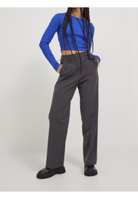 Crop top blu a maniche lunghe abbinato a pantaloni grigi a righe sottili con vestibilità rilassata e tasche laterali. Scarpe nere chunky completano il look.