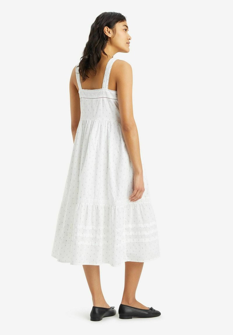 Weißes ärmelloses Kleid mit einem gestuften Design, verziert mit dezenten Mustern, mit strukturierten Details und einer fließenden, mittellangen Silhouette.
