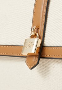 Canvas bag with tan leather accents, featuring a gold padlock detail and black trim. The texture is smooth with a sturdy design.