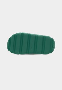 Σόλα πράσινου σανδαλιού slide με οριζόντιες αυλακώσεις και υφή λαβής, ορατή σε λευκό φόντο.