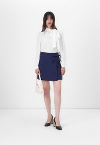 White blouse with a bow tie detail, paired with a navy mini skirt featuring two decorative bows, black heels, and a small pink handbag.