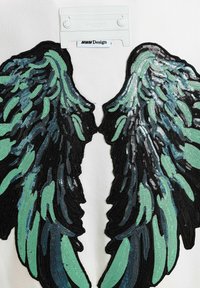 Prenda blanca con lentejuelas que presenta detallados diseños de alas en negro y turquesa. La textura es brillante con costuras visibles.