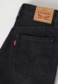 Poche de jean en denim noir avec un onglet rouge Levi’s et une étiquette en cuir beige Levi Strauss & Co. sur la ceinture.
