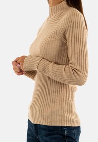Maglione beige a collo alto con maniche lunghe, tessuto testurizzato, design aderente e scollatura alta. Abbinato a jeans blu scuro.