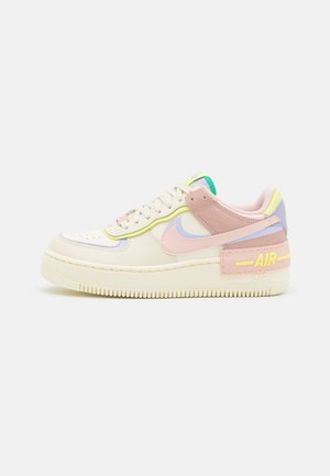 Baskets basses Nike Air couleur crème avec des accents rose pastel, lavande, jaune et vert, semelle épaisse et marquage « AIR » au talon.
