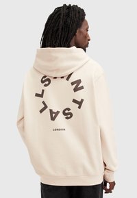 Hanorac roz deschis cu un logo circular mare, de culoare maro închis, care inscripționează "SAINT LAURENT" și "LONDON" în spate; material moale și croială lejeră.