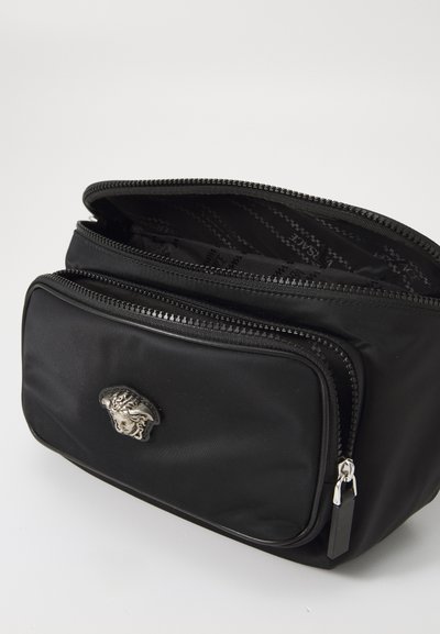 Črna najlonska kozmetična torbica z dvema zadrgama, ki vsebuje srebrno značko leva in gladko teksturo.