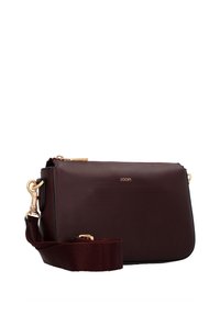 Burgundská kožená crossbody taška se zlatými prvky, zapínáním na zip a nastavitelným látkovým popruhem. Má minimalistický design a vytlačené logo.