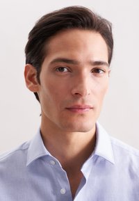 Camicia azzurro chiaro con colletto strutturato e texture morbida. La camicia presenta un solo bottone al colletto e una vestibilità rilassata.