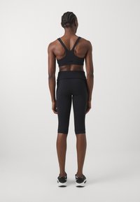 Completo sportivo nero composto da un reggiseno sportivo con spalline incrociate e leggings alla ginocchio, realizzato in materiale liscio e elastico con un design minimalista.