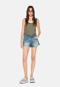 Top in cotone verde a costine, shorts in denim con effetto sbiadito e pantofole platform blu chiaro. Caratterizzato da una vestibilità aderente e uno stile casual.
