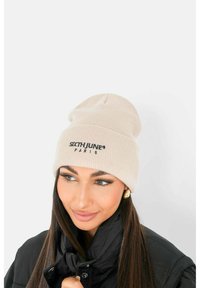 Beanie lavorato a maglia di un leggero beige con una vestibilità aderente e logo ricamato in nero. Texture liscia con design a risvolto.