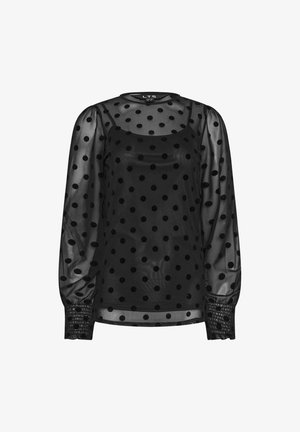 Zwarte doorschijnende blouse met lange pofmouwen, voorzien van grote, ronde zwarte stippen. Plissé-accenten bij de manchetten en een ronde halslijn.