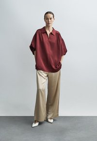 Bordo svilena bluza z ohlapnim krojem in kratkimi nabranimi rokavi, združena s kremnimi širokimi hlačami iz satenastega materiala in belimi čevlji z ostrim prstom.