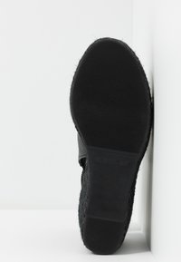 Suela de zapato negra con goma texturizada, que presenta una superficie suave y un logo grabado en el lateral. Perfil plano, ligeramente curvado en los bordes.