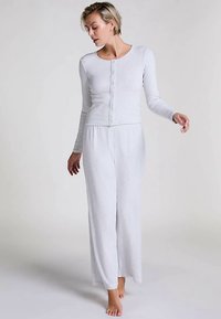 Lichtgrijs langermig shirt met knoopsluiting en bijpassende loszittende broek. Zacht materiaal met een gladde textuur. Casual lounge-set.