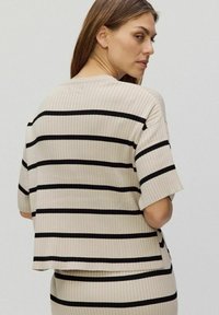 Beige randig ribbad topp med svarta horisontella ränder, med en avslappnad passform och korta ärmar, visad bakifrån.