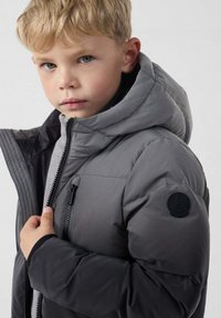 Chaqueta acolchada gris con capucha, con cierre frontal con cremallera, tejido texturizado y un parche de logo negro en la manga izquierda.