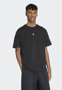 Sort bomulds t-shirt med rund hals, korte ærmer og et lille gult logo på den øverste del af brystet. Blød tekstur og afslappet pasform.