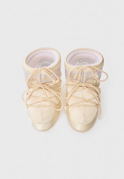 Stivaletti beige a metà altezza realizzati in materiale morbido, con punte rotonde, lacci frontali, colli imbottiti e un discreto marchio sui lati.