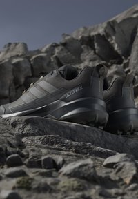 Chaussures de randonnée Adidas Terrex gris foncé sur terrain rocheux avec semelles robustes et tiges en mesh respirant.