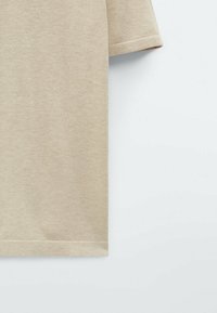 Short-sleeve beige shirt in a textured knit fabric. Features a straight hem and subtle stitch detailing at the sleeves.