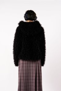 Fekete, bolyhos kapucnis dzseki, textúrált anyagból; hosszú, kockás szoknyával párosítva, amelyen borvörös és szürke vonalak vannak.