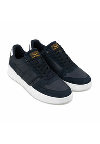 Marineblaue Sneakers aus Wildleder und Leder, mit einer weißen Gummisohle, flachen Schnürsenkeln und einem gelben Markenetikett an der Zunge.