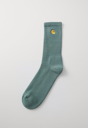 Calcetín de algodón verde con puño acanalado, que presenta un pequeño logotipo bordado en amarillo. Zona de los dedos sin costuras, textura suave y altura media.