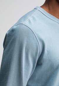 Hellblaues Baumwollhemd mit Rundhalsausschnitt, das über eine glatte Textur und eine Nahtverarbeitung am Kragen und an den Schulternähten verfügt.