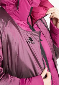 Fuchsia puffjacka med dragkedja fram, hög krage och texturerade ärmar med en broderad Adidas-logotyp på bröstet.