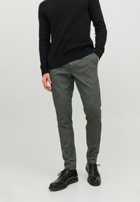 Pantaloni a righe grigie con una vestibilità slim, abbinati a un maglione nero a coste e scarpe nere. Il tessuto ha un aspetto strutturato.