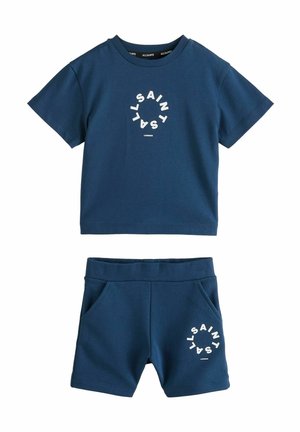 T-paita lyhyillä hihoilla, tummansininen ja siihen kuuluva shortsit pehmeästä kankaasta. Molemmissa osissa on ympyrän muotoinen valkoinen logo. Shortseissa on joustava vyötärö.