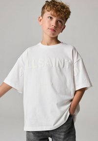 Bílé oversized tričko s vyraženým textem "ALLSAINTS" a "LONDON". Vyrobeno z bavlny, s krátkými rukávy a kulatým výstřihem.