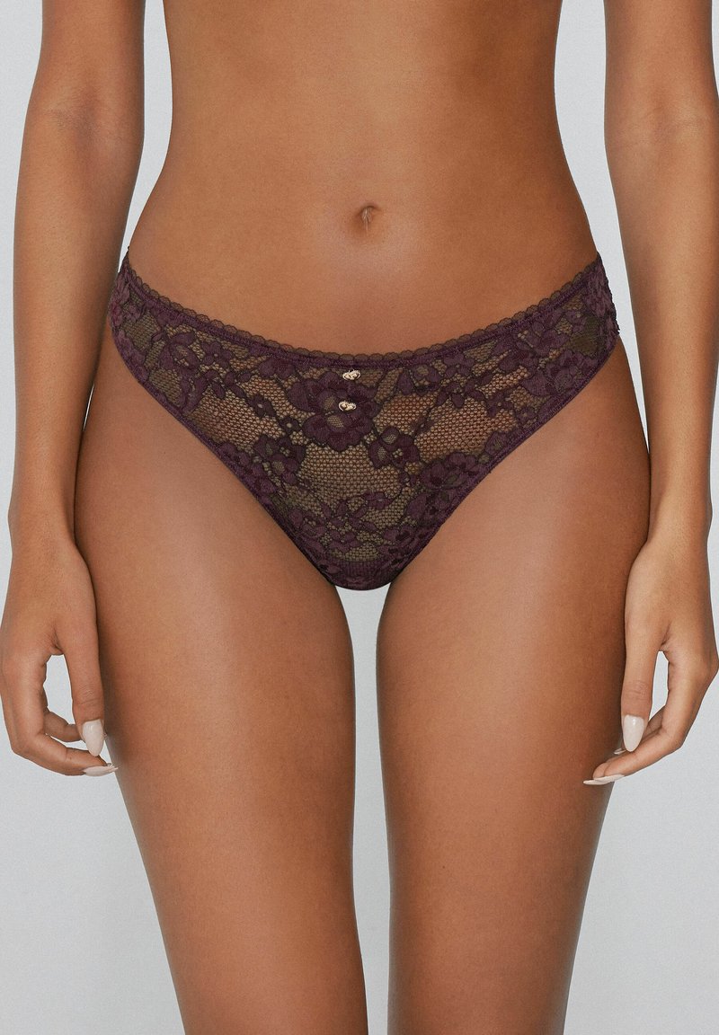 Spitzen-Thong in tiefem Burgunderrot, mit floralen Mustern und gewellten Kanten, verziert mit kleinen Akzenten aus goldfarbenem Metall am Bund.