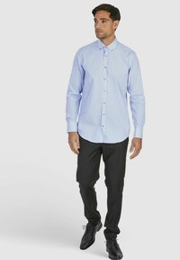 Lichtblauwe, langärmige overhemd met knopen en een geruit patroon, gecombineerd met zwarte pantalon en glanzende zwarte schoenen.