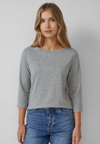 Chemise grise à manches longues avec un col rond, en tissu doux. Offre une coupe décontractée, à assortir avec un jean en denim bleu.