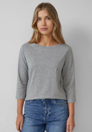 Chemise grise à manches longues avec un col rond, en tissu doux. Offre une coupe décontractée, à assortir avec un jean en denim bleu.