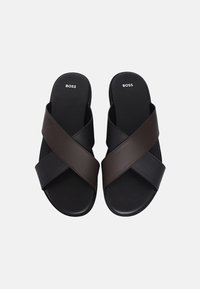 Czarne i brązowe sandały na krzyż z gładką teksturą i płaską podeszwą. Wewnątrz znajduje się logo, zaprojektowane z myślą o komforcie i codziennym noszeniu.