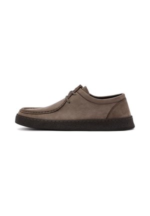Zapato de cuero marrón con perfil bajo, puntera redondeada y suela de goma negra gruesa. Presenta costuras mínimas y dos ojetes para el cordón.