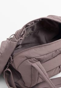 Odejen nahrbtnik iz vijoličnega blaga z zadrgo, ki ima prostorno notranjost in stranske žepe, zasnovan za udobje in uporabnost.