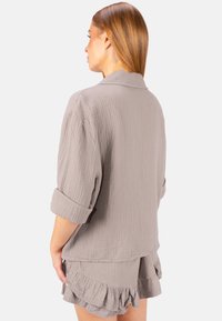 Hellgraues Shirt mit Waffelstruktur und hochgekrempelten Ärmeln, kombiniert mit passenden Shorts mit Rüschensaum. Schlichte, entspannte Silhouette.