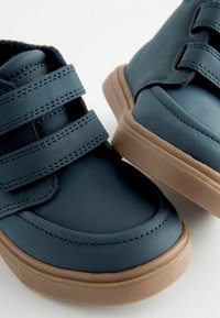 Chaussures en cuir bleu avec semelles en caoutchouc brun, dotées de deux sangles Velcro réglables et d'une finition lisse, mettant en valeur des détails de couture minimalistes.