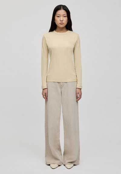 Beige Langarmshirt mit Rundhalsausschnitt, kombiniert mit hellen, weiten Jeans und beigen Schuhen mit spitze. Schlichtes Design.