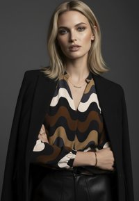 Braune, cremefarbene und marineblaue Bluse mit Wellenmuster und Kragen, kombiniert mit einem schwarzen Blazer und Lederhosen. Dezente goldene Schmuckakzente.