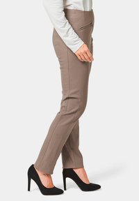 Beige broek met een slim fit, ritsvak aan de zijkant en parallelle stiksels die naar beneden langs de voorkant lopen. Gecombineerd met zwarte hoge hakken.