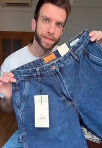 Bermudas de ganga azul com um ajuste padrão, apresentando um botão de cobre, uma etiqueta de couro e duas etiquetas presas à cintura.